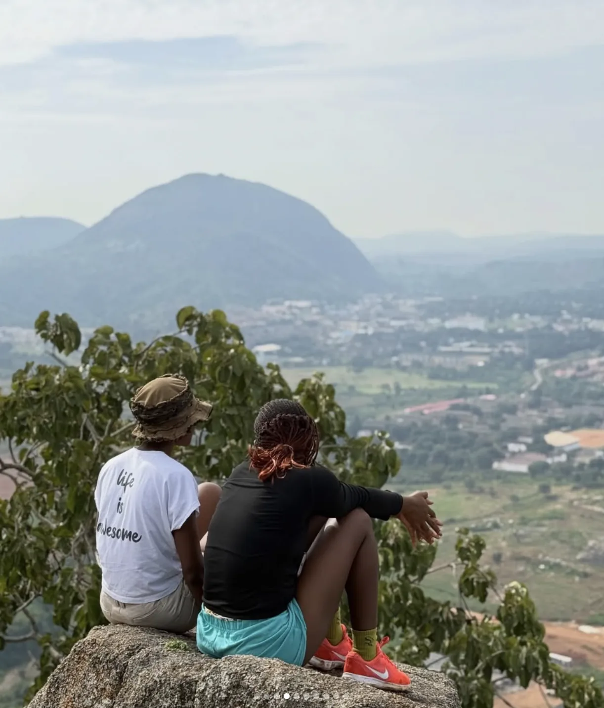 Two explorers sitting on a rock overlooking Nigerian mountains